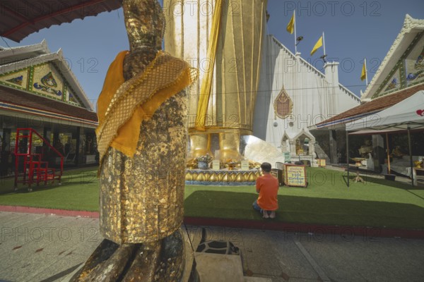 Man praying in front of a 32 metre high standing Buddha decorated with glass mosaics and 24 carat gold, Luang Pho To or Phrasiariyametri, Wat Intharawihan, Bangkok, Thailand