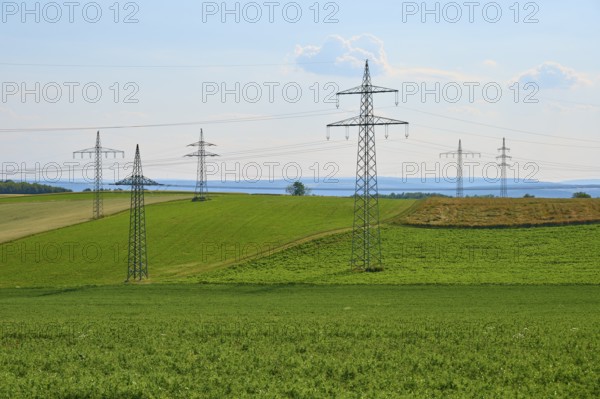 Green fields with a row of electricity pylons under a blue sky, Marktheidenfeld, Bavaria, Germany