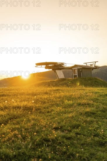 Sunset over a green meadow with a silhouette of a cable car station, Alpe di Siusi, Dolomites, South Tyrol, Italy