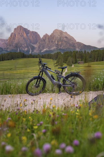 E-bike on a gravel road in front of the imposing silhouette of the Dolomites in the evening light, Alpe di Siusi, Sassolungo Group, Dolomites, South Tyrol, Italy