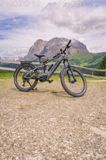 An e-bike stands on a gravel path in front of a mountain landscape, Alpe di Siusi, Dolomites, South Tyrol, Italy