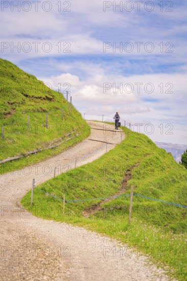 Motorcyclist on a winding gravel road in a hilly landscape, Alpe di Siusi, Dolomites, South Tyrol, Italy