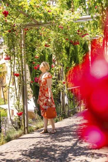 Woman in a red dress walks through a flowering garden pavilion, surrounded by green foliage, Botanical Garden, The Gardens of Trauttmansdorff Castle, Merano, South Tyrol, Italy