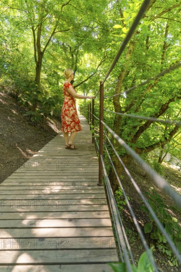 A woman on a wooden footbridge in the forest, surrounded by green trees, Botanical Garden, The Gardens of Trauttmansdorff Castle, Merano, South Tyrol, Italy