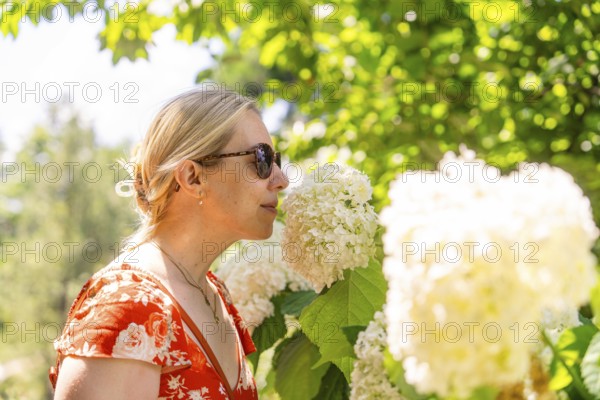 Woman in a red dress smelling a white flower, surrounded by green plants, Botanical Garden, The Gardens of Trauttmansdorff Castle, Merano, South Tyrol, Italy