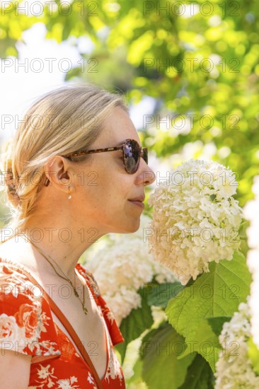 Woman smelling a white flower, surrounded by green plants, wearing a red dress, Botanical Garden, The Gardens of Trauttmansdorff Castle, Merano, South Tyrol, Italy