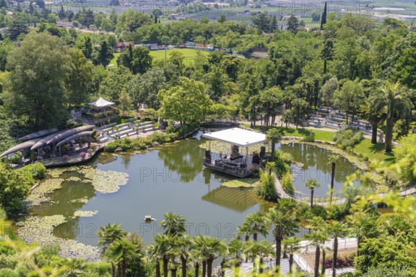 A pond with a pavilion in the middle of a green park, surrounded by landscape, Botanical Garden, The Gardens of Trauttmansdorff Castle, Merano, South Tyrol, Italy
