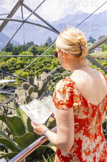 Woman in a red dress looking at a map near a structural glass construction, Botanical Gardens, The Gardens of Trauttmansdorff Castle, Merano, South Tyrol, Italy