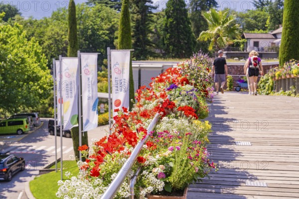 Flowerbeds along a wooden path with flags and walkers, Botanical Garden, The Gardens of Trauttmansdorff Castle, Merano, South Tyrol, Italy