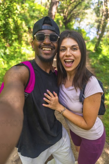 Happy couple taking a selfie while hiking on a forest trail, enjoying the beautiful nature surrounding them
