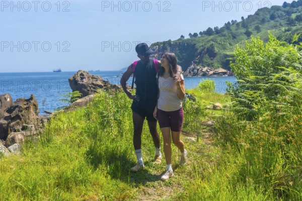 Interracial couple walking along a coastal path, enjoying the scenic views of the ocean and green landscape