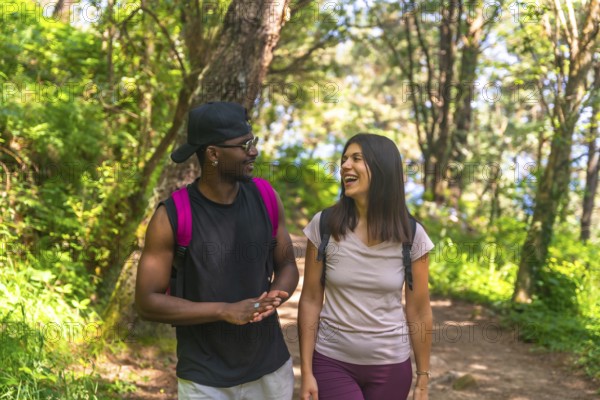 Two hikers with backpacks are enjoying a conversation while walking on a trail through a lush green forest