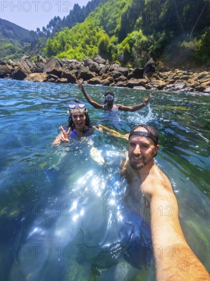 Three friends enjoy snorkeling in the refreshing ocean water, capturing a selfie moment amidst a beautiful coastal landscape