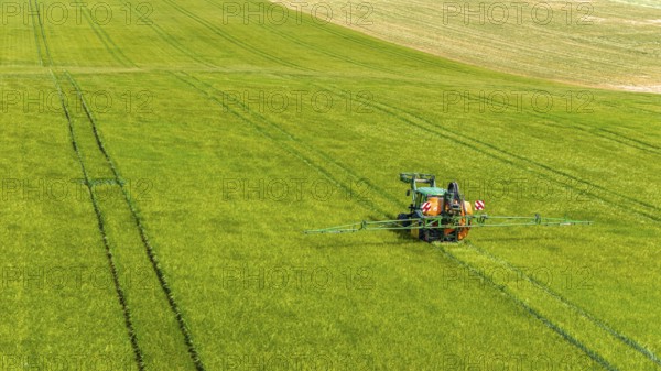 Farmer with tractor working in the field. In early summer, he fertilises the grain for an optimum yield. Drone photo. Merklingen, Baden-Württemberg, Germany