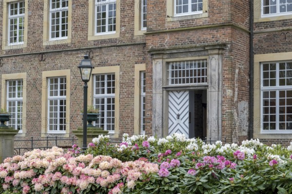 Brick building with large entrance door, blooming rhododendrons and an old lantern in the foreground, moated castle Haus Welbergen, Ochtrup-Welbergen, Münsterland, North Rhine-Westphalia, Germany