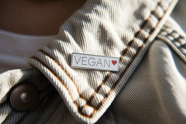 Close-up of silver pin with VEGAN text and red heart on worn cotton jacket. Symbol of ethical lifestyle and compassionate choice. Generative ai, AI generated