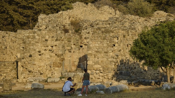 Two people in front of an old stone wall in a setting surrounded by trees, Roman bathhouse, Asklipion, Asklepieion, healing temple, temple, Hippocrates, Kos, Dodecanese, Greek Islands, Greece