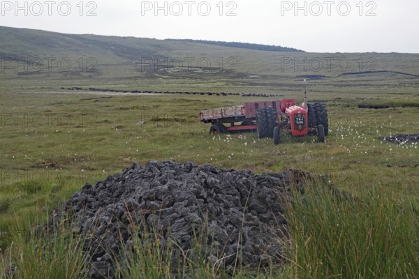 Old red tractor standing in boggy fields against a hilly backdrop with grey sky, peat cutting, Isle of Harris, Hebrides, Scotland, United Kingdom