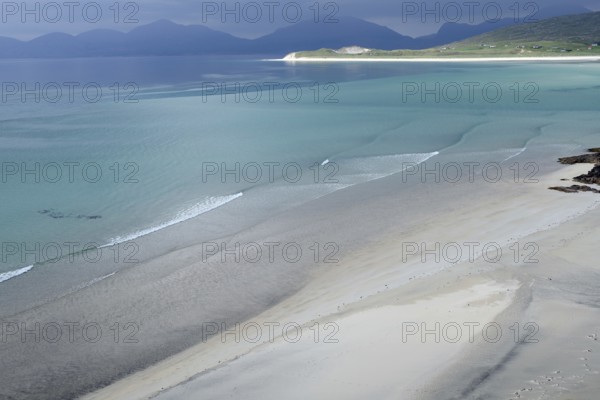 Gentle waves roll over fine sand against a majestic backdrop of mountains and calm sea, Seilebost Beach, Isle of Harris, Hebrides, Scotland, United Kingdom