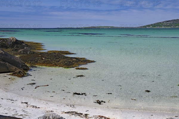 Tranquil beach landscape with rocks, sea and clear blue sky with seaweed on the shore, Eriksay, Hebrides, Scotland, United Kingdom