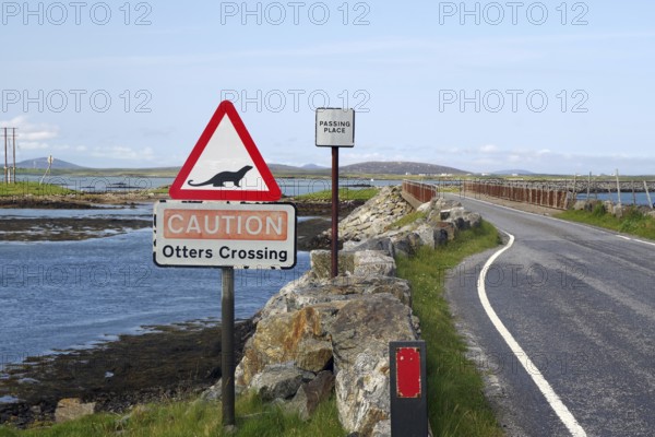 Road scene with otter crossing warning sign, coast and bridge in rural setting, causeway, Benbecula, cycle tour, North Uist, Hebrides, Scotland, Great Britain