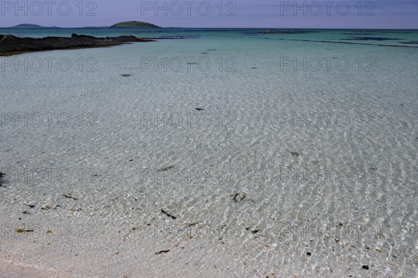 Crystal clear turquoise water on a sandy beach with islands on the horizon under a blue sky, Eriksay, Hebrides, Scotland, United Kingdom