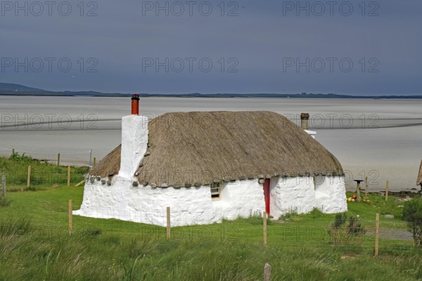 White thatched house on a green meadow against a sandy coastal background under a blue sky, holiday, holiday home, North Uist, Hebrides, Scotland, Great Britain