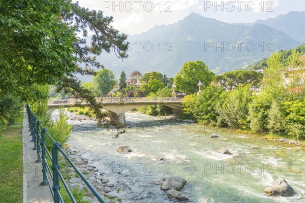 River with a bridge and mountainous landscape under a clear sky, Merano, Italy
