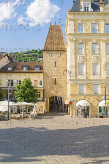 Historic square with a medieval tower and surrounding buildings, illuminated by the warm summer sun, Merano, Italy