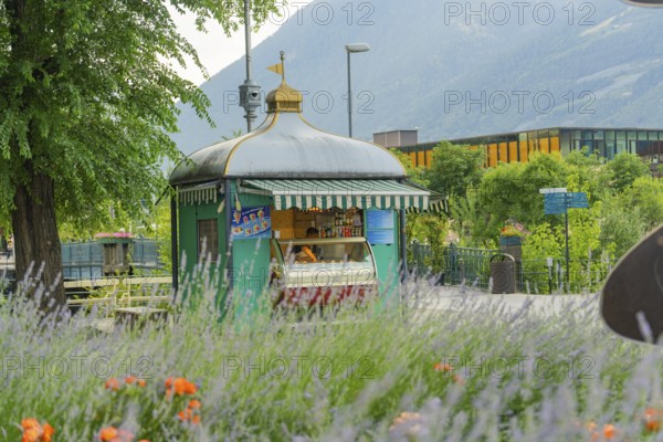 Small kiosk in a scenic park setting with mountains and flowers, Merano, Italy