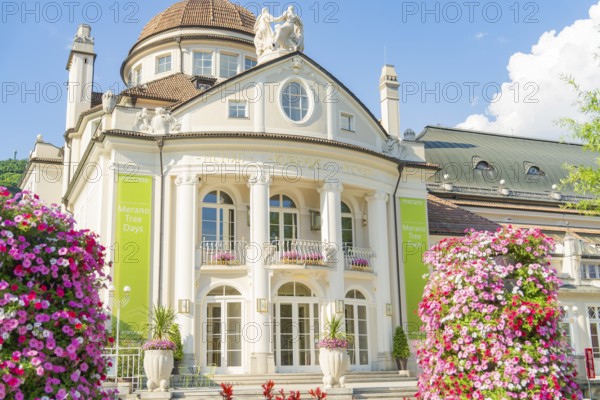 A magnificent baroque building with flowerbeds and flowering plants in the foreground, Merano, Italy