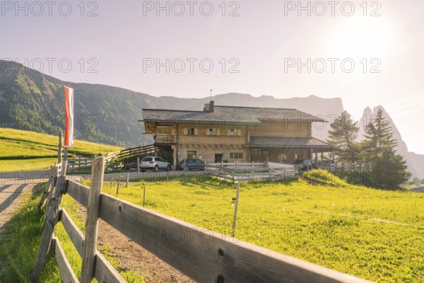 Large farmhouse with wooden fence on a wide green field in a sunny mountain landscape, Alpe di Siusi, Dolomites, South Tyrol, Italy