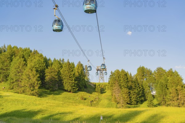 Cable car over green meadows and dense forests under a clear sky, Alpe di Siusi, Dolomites, South Tyrol, Italy