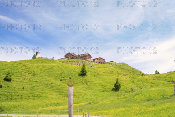 Wooden building on a green hill in front of a blue sky with white clouds, Alpe di Siusi, Dolomites, South Tyrol, Italy