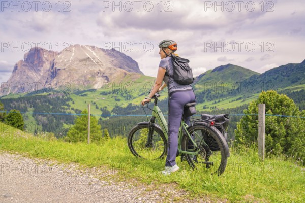 Cyclist on a path with a view of a mountain landscape under a cloudy sky, Alpe di Siusi, Dolomites, South Tyrol, Italy