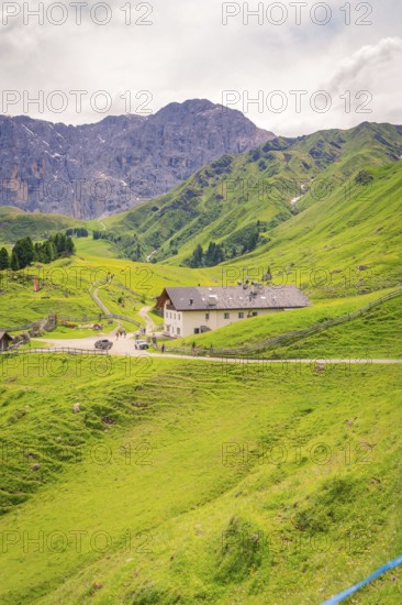 Large building nestled in a green mountain landscape under a cloudy sky, Alpe di Siusi, Dolomites, South Tyrol, Italy