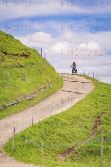 A cyclist rides on a winding hilly path in sunny weather, Alpe di Siusi, Dolomites, South Tyrol, Italy