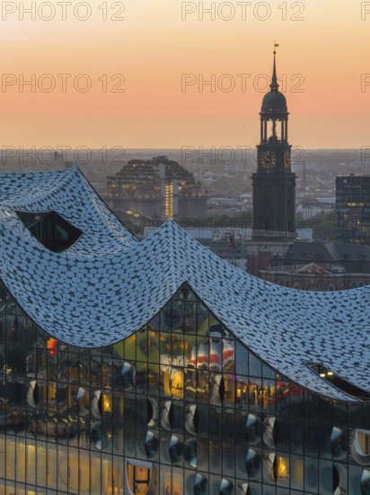 Aerial view of the Elbphilharmonie at sunset with illuminated windows and view over Hamburg and the main church St Michaelis (Michel), Hamburg, Germany