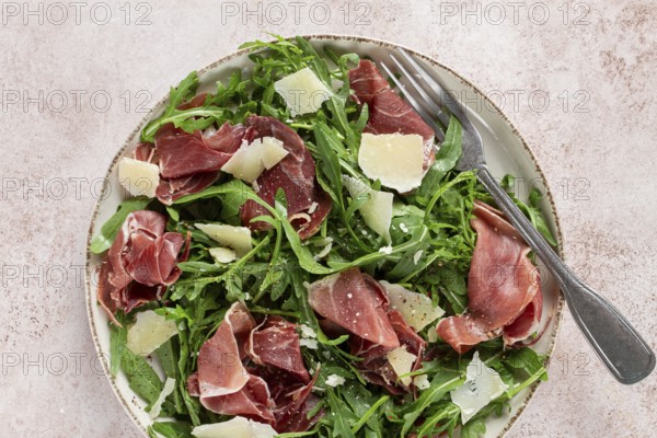 Fresh arugula salad with prosciutto and grated parmesan cheese, on a plate, homemade, no people