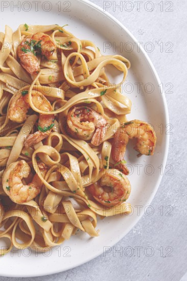 Fettuccine pasta with shrimp, spicy in soy sauce, on a grey plate with a fork, close-up
