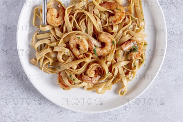 Fettuccine pasta with shrimp, spicy in soy sauce, on a grey plate with a fork, close-up