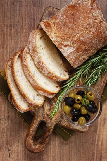 Sliced ciabatta, on a chopping board, with rosemary and olives, Italian bread, close-up, Italian cuisine, breakfast, no people