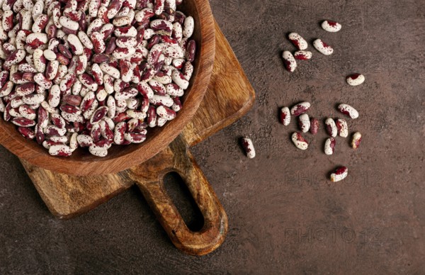 Variegated beans, red with white spots, raw in a wooden bowl, top view, no people