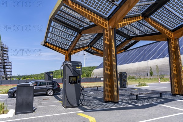 Electric charging station on the site of the former Lohberg colliery in Dinslaken, operated by Fastned, uses electricity from wind power and solar energy, fast-charging columns, with its own solar roof, in the background the 11, 500 square metre solar roof on the colliery's former coal mixing hall, wind farm on the Lohberg slagheap, North Rhine-Westphalia, Germany