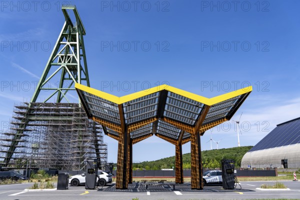 Electric filling station on the site of the former Lohberg colliery in Dinslaken, operated by Fastned, uses electricity from wind power and solar energy, fast-charging columns, with its own solar roof, in the background the 11, 500 square metre solar roof on the colliery's former coal mixing hall, wind farm on the Lohberg slagheap, Lohberg colliery headframe, North Rhine-Westphalia, Germany