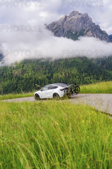 A car on a path with towering mountains in the background and damp fog, electric car on holiday, Dolomites, South Tyrol, Dolomites, Italy