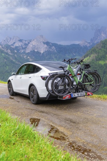 White car with bicycles on wet road, surrounded by mountains and rain clouds, electric car on holiday, Dolomites, South Tyrol, Dolomites, Italy