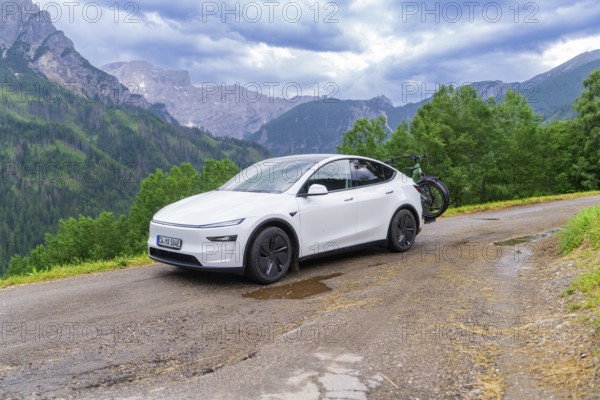 White car with bicycles on a winding mountain road, surrounded by dense greenery and cloudy sky, electric car on holiday, Dolomites, South Tyrol, Dolomites, Italy