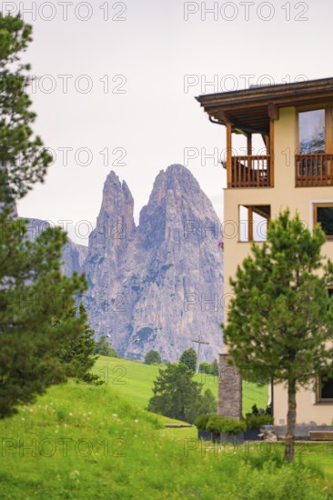 View of impressive rock formations behind a building with green foreground, Alpe di Siusi, South Tyrol, Dolomites, Italy
