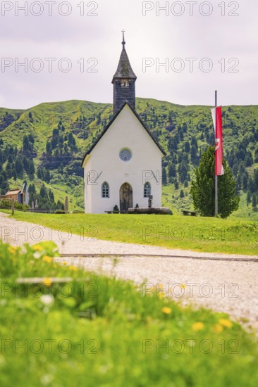 White church stands idyllically on a green meadow with mountain backdrop and flag, Alpe di Siusi, South Tyrol, Dolomites, Italy